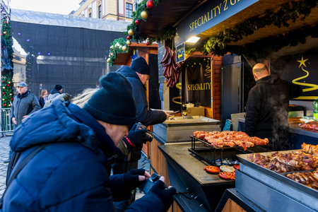Grilled meat stand at a Christmas market with customers in the foreground. Christmas market, featuring a food stand specializing in grilled meat and sausages in the foregroundのeditorial素材