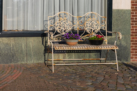 Detail of a white metal bench with blooming flowers in front of a house in Bedum. Morning sun and shadows on a Dutch street.の写真素材