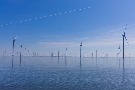 Modern offshore wind turbines on calm sea water under a clear blue sky. Sustainable energy in the...