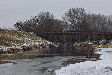 Breathtaking shots of a frozen dam. Massive ice formations, icicles, and frozen waterfalls covering the weir structure. The contrast between flowing water and thick ice creates a dramatic winter landscape under a sunset skyの写真素材