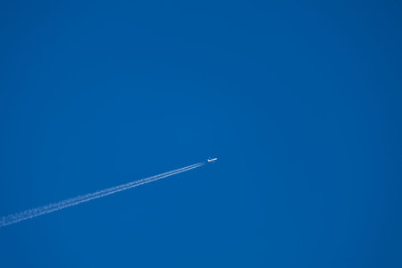 A minimalist high-altitude shot of a commercial jet aircraft flying through a clear, deep blue sky....