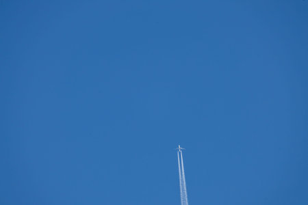A bottom view of a commercial jet airplane flying at high altitude in a clear, deep blue cloudless...