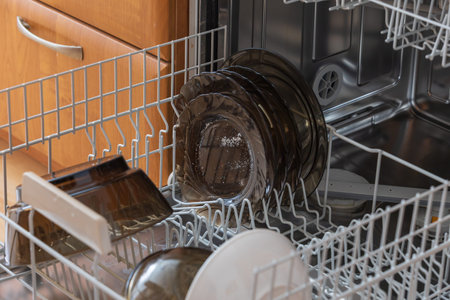 A high-angle view showing a loaded dishwasher rack with dark translucent dishes ready to be put away. This lifestyle image represents daily household chores, efficiency in the kitchen, and modern domestic organization.