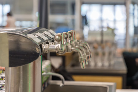 High-angle close-up of sleek chrome draft handles and spouts, emphasizing a clean and efficient self-service beverage station. The blurred background suggests a busy, contemporary commercial environment with a focus on hygiene and modern hospitality design.