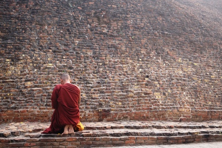 Buddhist monk kneeling to pray at the Buddha's cremation stupa in a foggy morning, Kushinagar, India