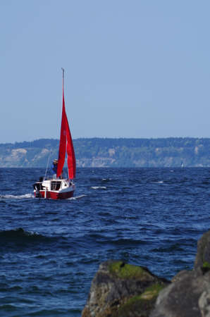 Sailboat with red sails tacking off Edmonds Marina on Puget Soundの写真素材