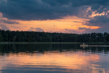 the man on the boat flows through the lake in the light of the setting sunの写真素材