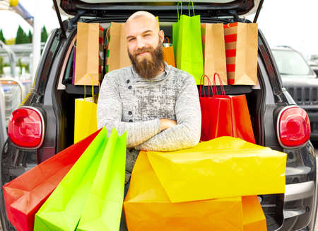Smiling man having fun with lots of bags on a shopping day for the black friday. Concept about how...