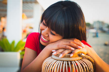 beautiful smiling asian girl with brunette hair and red shirt sitting in lounge bar at sunset on the beach.concept about joy and happiness, laughing a lot.の写真素材