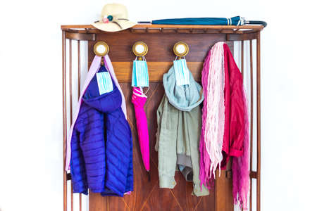 winer jackets and umbrellas hanging on the clothes hanger with protective face masks..coats and hat hanging on the wall.concept about new normal lifestyle after reopening post lockdown.focus on the masks above the umbrellaの写真素材