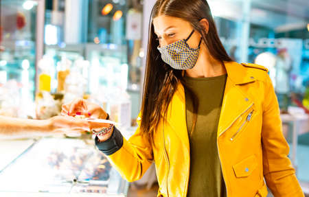 Young and happy woman wearing protective face mask getting a white chocolate standing inside a shop.girl having a sweet candy in autumn after lockdown reopening.concept about joy and hapiness.new normal lifetstyle.の写真素材