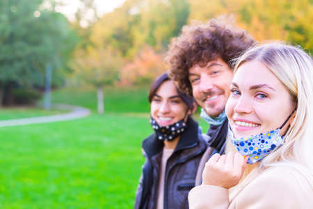 Young people having fun around city park during coronavirus outbreak-Happy multiethnical friends wearing face protective masks and laughing together.Main focus on right girl face.concept about new normal lifestyleの写真素材