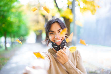 Close up portrait of a Beautiful brunette girl wearing protective face mask standing near colorful autumn leaves. Art work of romantic woman. Pretty tenderness model looking at camera after lockdown reopening.new normal lifestyleの写真素材