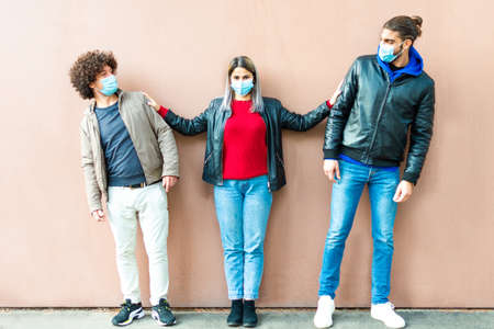 happy group of friends wearing protective face mask keeping social distances after the lockdown reopening. two men and a woman pushing them aside for a portrait photo on a smooth colorful background.concept about responsibility in the new normal lifestyleの写真素材