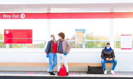 group of a man and a couple wearing protective face mask in a train station waiting for the bus keeping social distances.people standing on a metro stop after reopening post lockdown.concept about responsibilty in the new normal lifestyle and travel rulesの写真素材