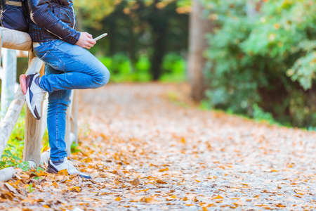 man interacting with smartphone app on a winter day.Beautiful autumn landscape with leaves road.Colorful foliage in the park.Falling leaves natural background.orange and yellow.concept about tech, traveling and connectionの写真素材