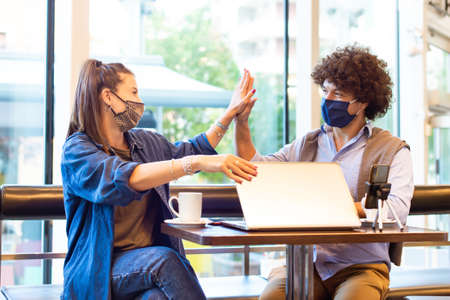 Young millenial students giving each other an high five after done studying and video calling on a...