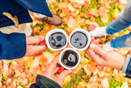 young friends toasting with coffee mug oudoors in a park.red and orange mood.Beautiful landscape with yellow leaves and Colorful foliage in the forest.mood of joy and togetherness while chilling and relaxingの写真素材