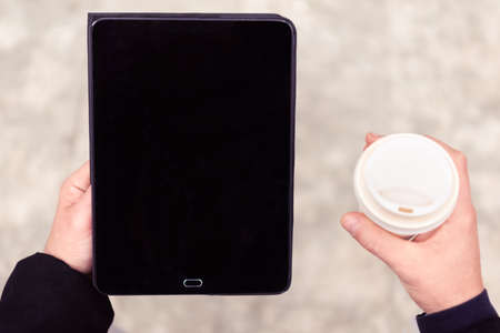 close up portrait of a business man holding a tablet device and carrying his coffee during a work meeting break.background up view image of a black kindle laptop.concept about tech, social and online connectionの写真素材