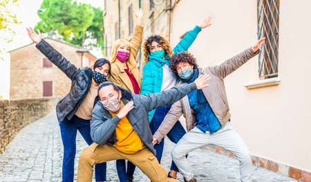 smiling happy group of friends having fun in a city street wearing warm winter clothes and protective face mask to celebrate coronavirus lockdown reopening.の写真素材