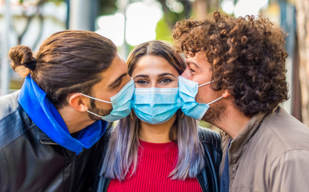 close up portrait of two man and a caucasian woman kissing each other wearing protective face mask outdoor after coronavirus lockdown reopening holidays.friends in a sweet moment.new normal lifestyleの写真素材