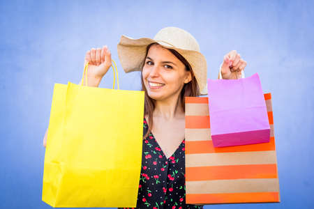 close up portrait of a young beautiful woman standing on colorful background wall holdind shopping bags on a summer sales.happy and joyful caucasian girl smiling at camera after shop.lifestyle conceptの写真素材
