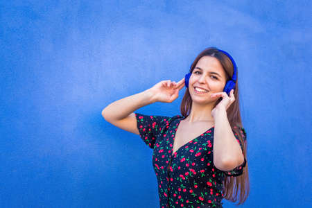 happy wonderful woman wearing headphones standing against a colorful background.Smiling beautiful girl listening to music wearing summer clothes.tech, joy, relax and chilling concept.close up portrait.の写真素材