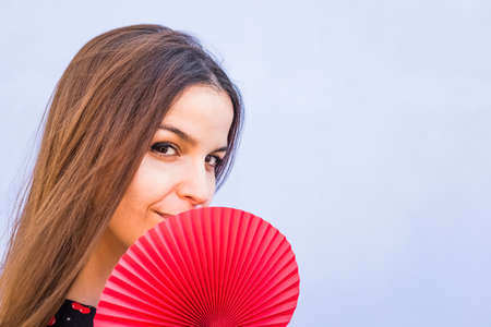 close up portrait of a wonderful caucasian woman holding a colorful folding fan.gorgeous side view of a happy brunette girl isolated on a background looking at camera.intense look, sensuality conceptの写真素材