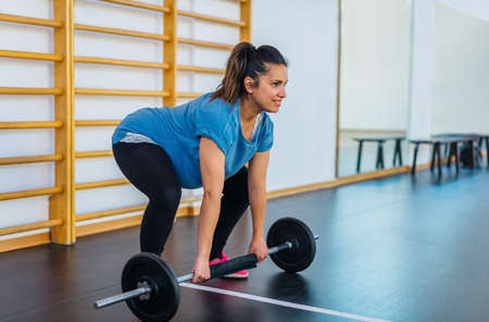 beautiful pregnant woman with a nice smile alone doing workout exercise indoor.happy girl lifting weight in a gym session inside.fit, training, fitness, health concept.one person doing train routine.の写真素材