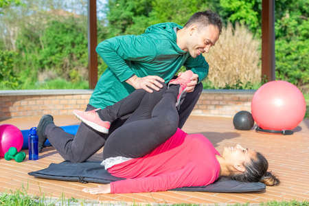 couple of a smiling personal trainer and a beautiful woman doing workout exercise outdoor.friends practicing stretching after gym session outside. fit, training, fitness, health and friendship conceptの写真素材