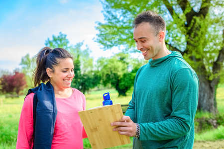 couple of personal trainer and a young student woman discussing training schedule together smiling outdoor.fitness and healthy lifestyle concept about workout, fit, friendship and fit journey in a parkの写真素材