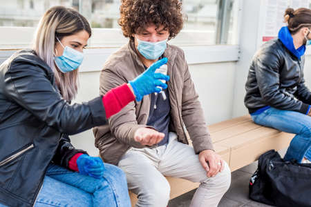 young couple waiting in tram station using sanitizer hand gel wearing protective face mask, gloves during  lockdown reopening.virus outbreak concept, new normal lifestyle.friends travelingの写真素材