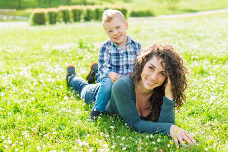 happy mom and child chilling in public park garden in summer.smiling mother and son relaxing toghether outdoor laying on grass.togetherness, love, family and happiness concept.sunlight effect.piggybackの写真素材