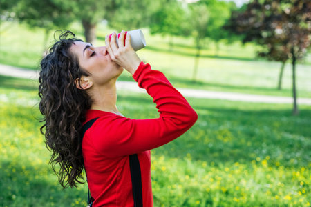 Beautiful woman drinking coffee to go in a park outdoor in summer. Portrait of young adult girl...