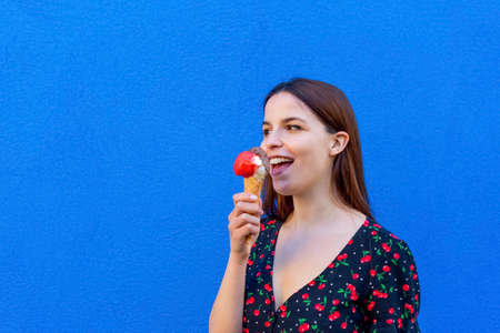 indoor close up fashion portrait of young hipster girl eating ice cream in summer isolated on blue...