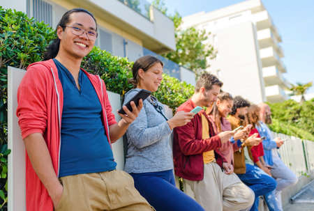 multiethnic group of friends in the street outdoors interacting with smartphones on social media laughing and having fun. diverse people together on happy holidays. technology and lifestyle conceptの写真素材