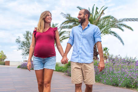 young happy couple in love of a pregnant woman and her boyfriend walking on the street having fun on holidays. quality family time holding hands on vacation days. joy, big belly and lifestyle conceptの写真素材