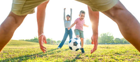 young happy family playing football outdoors into a public park garden. mom, dad and little child having fun together. cute kid kicking a ball in motion scoring a goal. sport and lifestyle conceptの写真素材