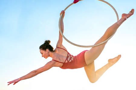 acrobat athletic, young graceful gymnast performing aerial exercise in the air ring outdoors on sky...