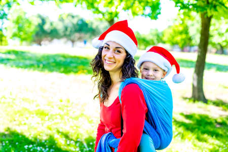merry christmas! Young family portrait celebrating xmas time wearing santa claus hat standing outdoors in park. mother and child chilling together. family time and lifestyle concept on winter holidaysの写真素材
