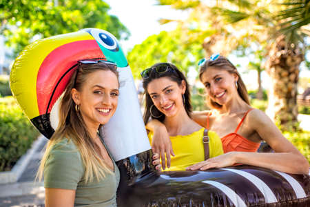 group of beautiful women portrait on summer vacation holiday carrying inflatable toucan mattress on the street having fun together hugging each other. friends travel journey walking. lifestyle conceptの写真素材