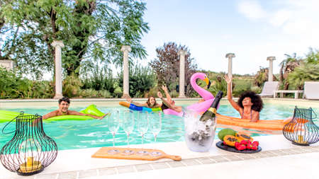 summer swimming pool party! happy multiracial group of friends relaxing on inflatable mattress having drinks celebrating hot holidays outdoor. people having wine on happy hour. lifestyle conceptの写真素材