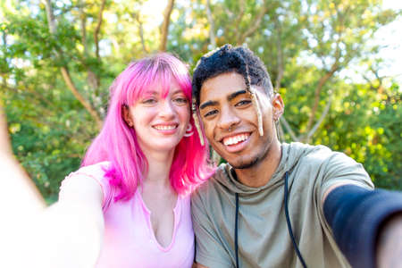 different alternatives couple hanging out in a park making a pov selfie portrait holding smartphone...