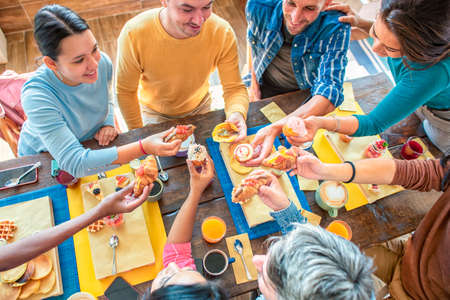 cropped top of multiethnic large group of friends at cafe table restaurant eating muffin and cakes. diverse people celerating sweet breakfast together enjoying happy holiday. lifestyle and joy conceptの写真素材