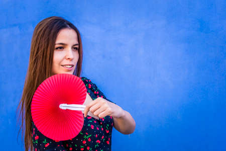 close up portrait of a wonderful caucasian woman holding a colorful folding fan. gorgeous side view of a happy brunette girl isolated on a background looking at camera. summer mood lifestyle conceptの写真素材