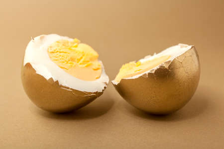 Boiled egg cut in two pieces, painted gold over beige backgroundの写真素材