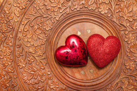 Two red hearts over a carved wooden tableの写真素材
