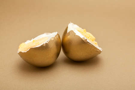 Boiled egg cut in two pieces, painted gold over beige backgroundの写真素材