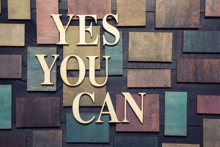 Wooden letters forming words YES YOU CAN written on wooden background