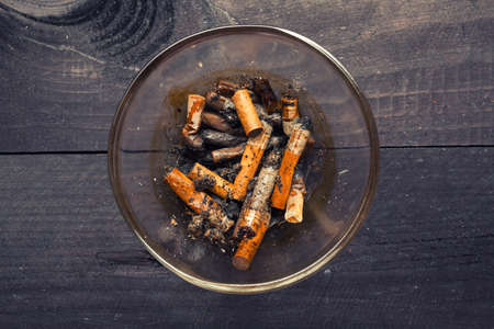 Dirty cigarette butts in a glass ashtray on wooden tableの写真素材